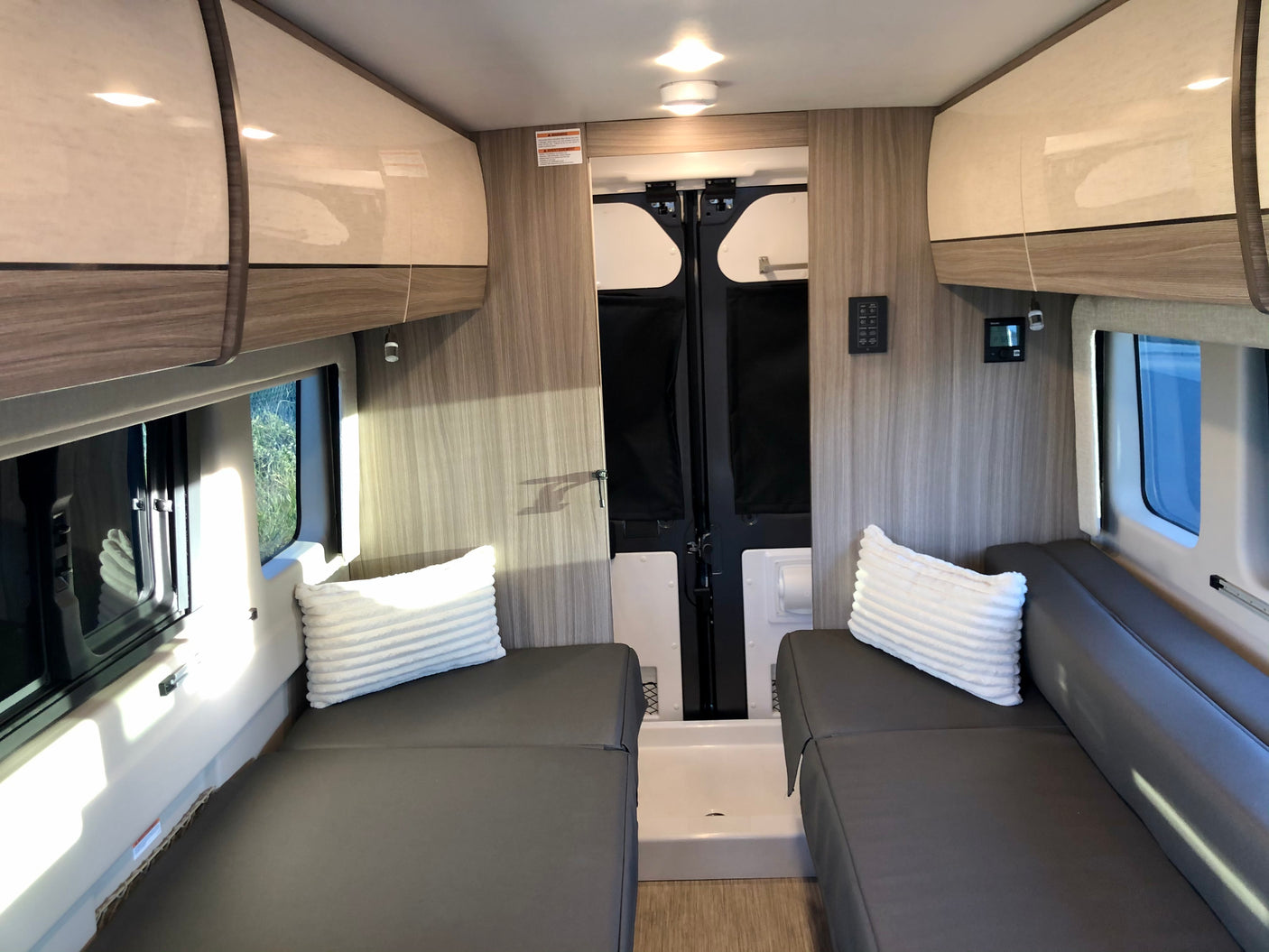 RV rental interior: twin beds flank a central aisle leading to a rear wet bath. Overhead cabinets, windows.