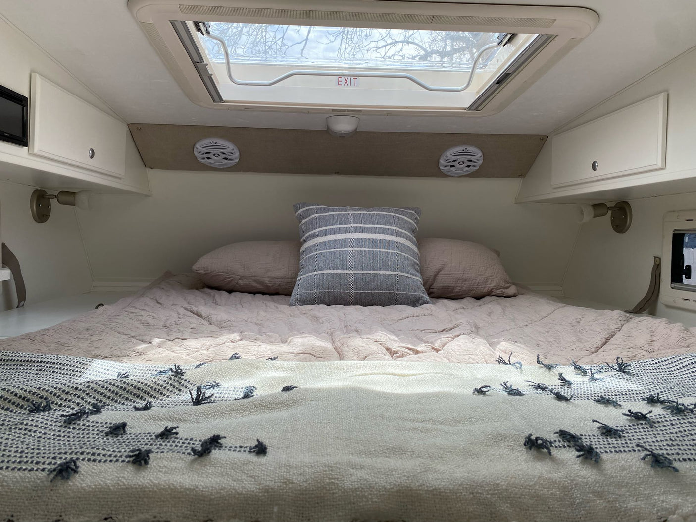RV rental interior showing a snug bed with soft bedding, pillows, and an overhead exit skylight.