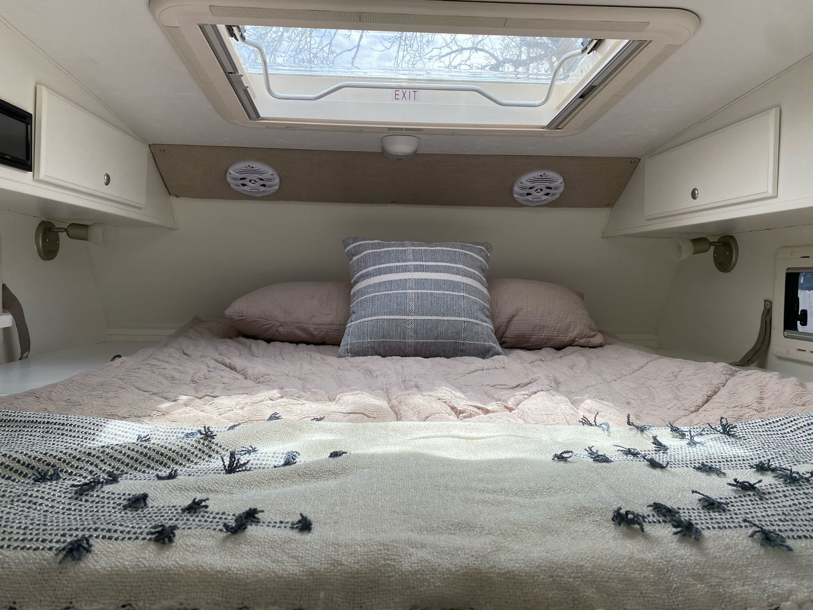 RV rental interior showing a snug bed with soft bedding, pillows, and an overhead exit skylight.