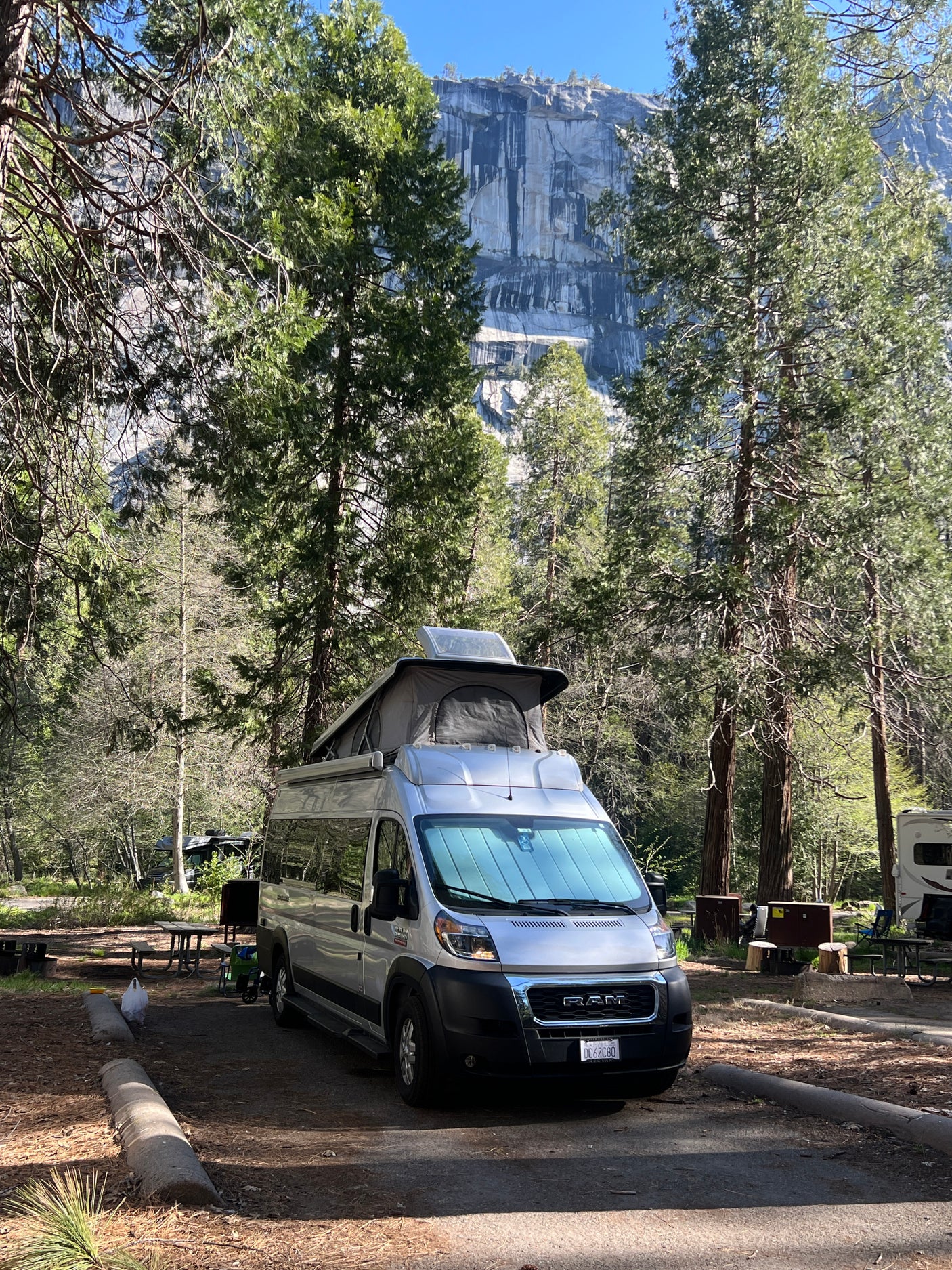 Silver camper van with pop-top at a scenic mountain campsite, ideal for an rv rental adventure.