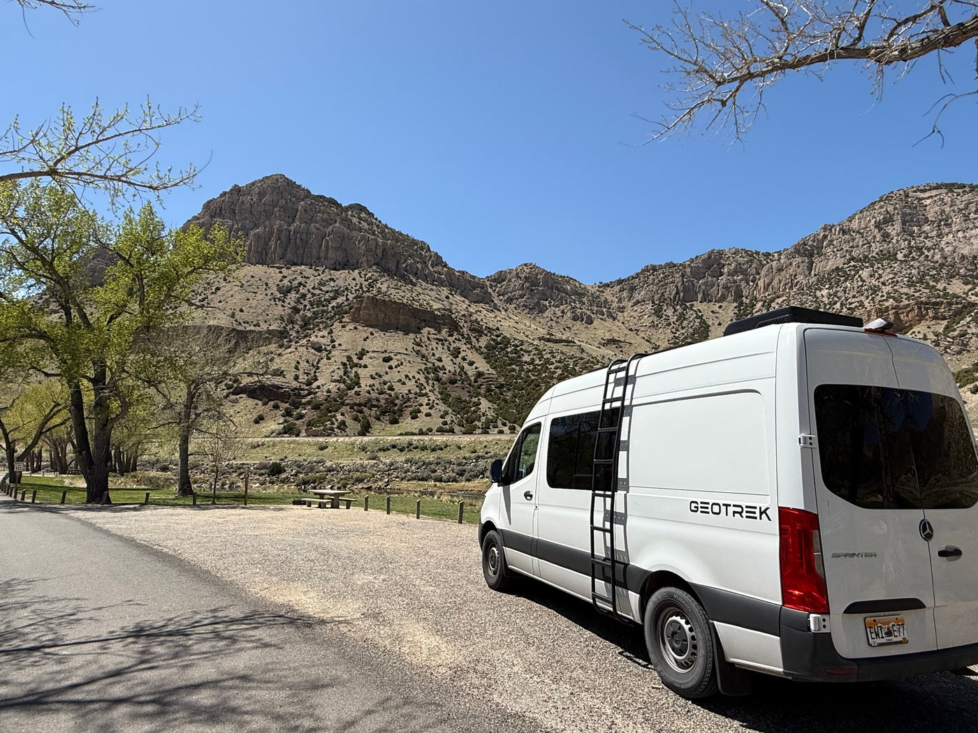 White GEOTREK rv rental parked in a beautiful mountain campsite with fresh spring trees under a clear sky. — photo 14