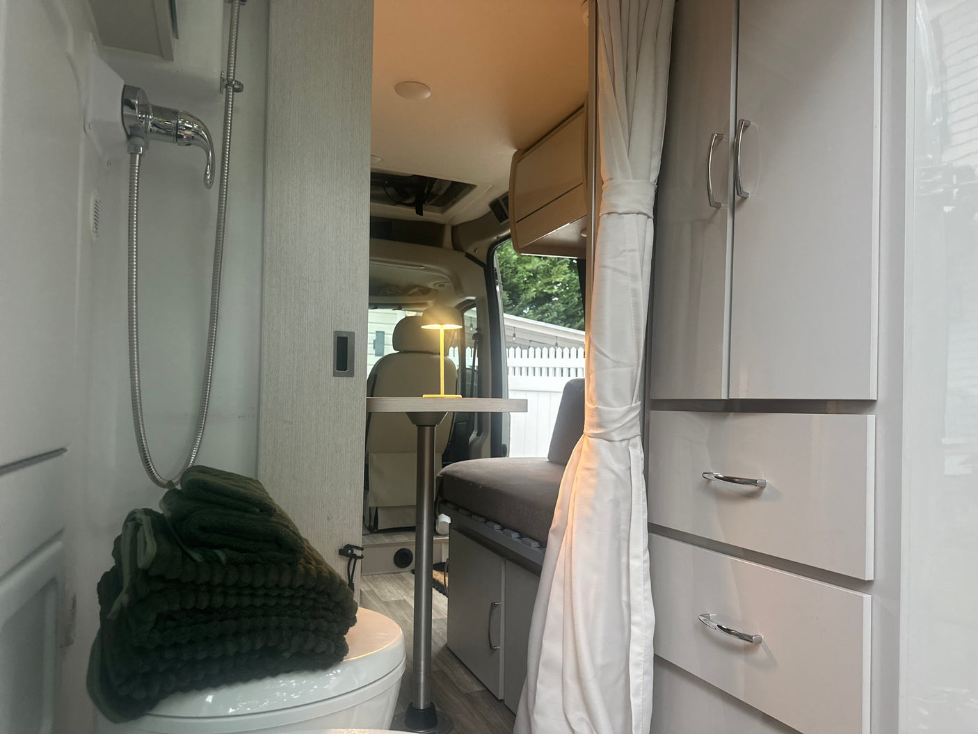 Explore this compact RV rental interior: integrated shower/toilet, dining table with lamp, and storage cabinets for comfy travel.