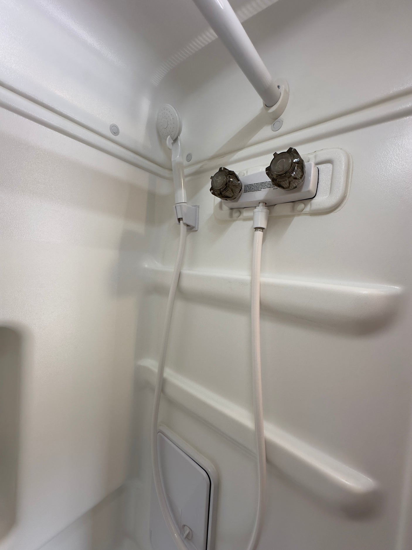 Inside an RV rental shower: white molded walls, handheld shower, dual faucets, grab bar, and integrated storage.