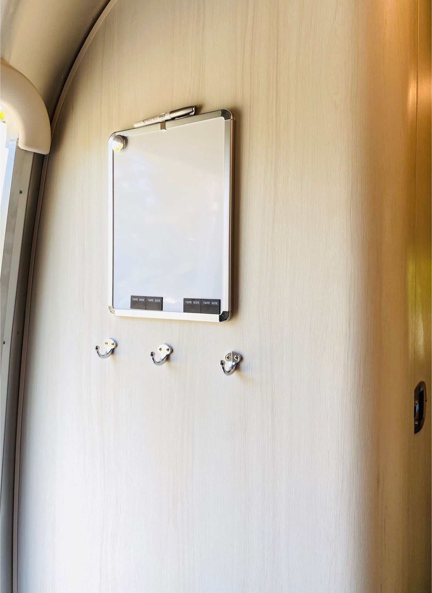 RV rental interior: A practical whiteboard with marker and three hooks on a light wood-grain wall.