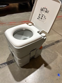 A gray portable chemical toilet with an open lid & white seat. Essential for RV rental camping sanitation.