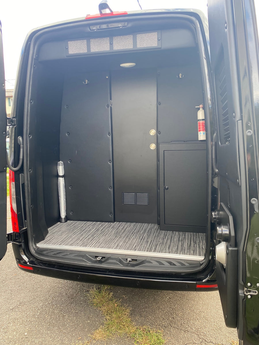 View inside a black RV rental van. Custom interior panels, a storage door, safety gear, and patterned flooring.