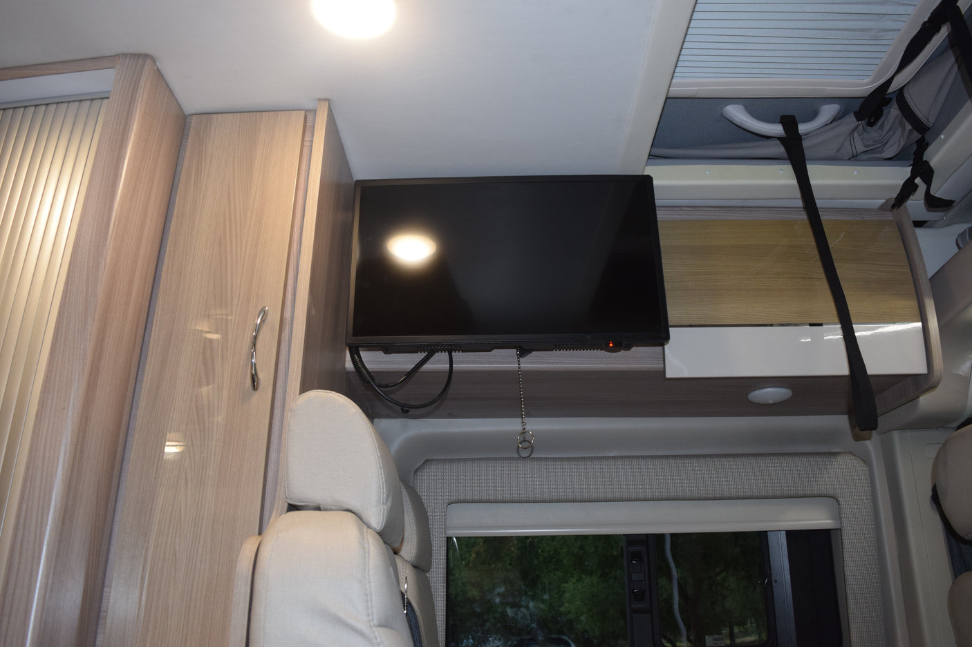 RV rental interior with a mounted TV, light wood cabinets, comfortable seating, and overhead storage.