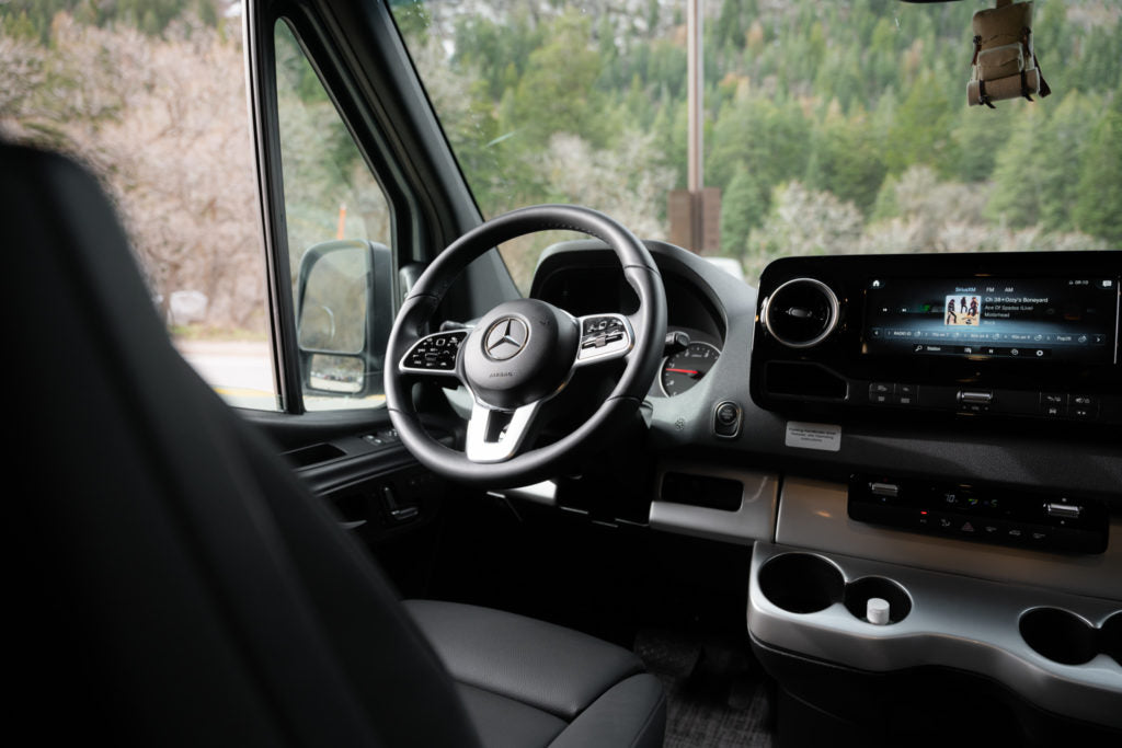 Interior of a modern Mercedes-Benz RV rental, showing the driver's seat, steering wheel, and dashboard display.