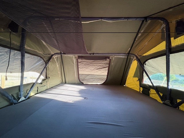 Inside an rv rental rooftop tent: a cozy sleeping area. Features mattress, screen windows, & storage net for camping.