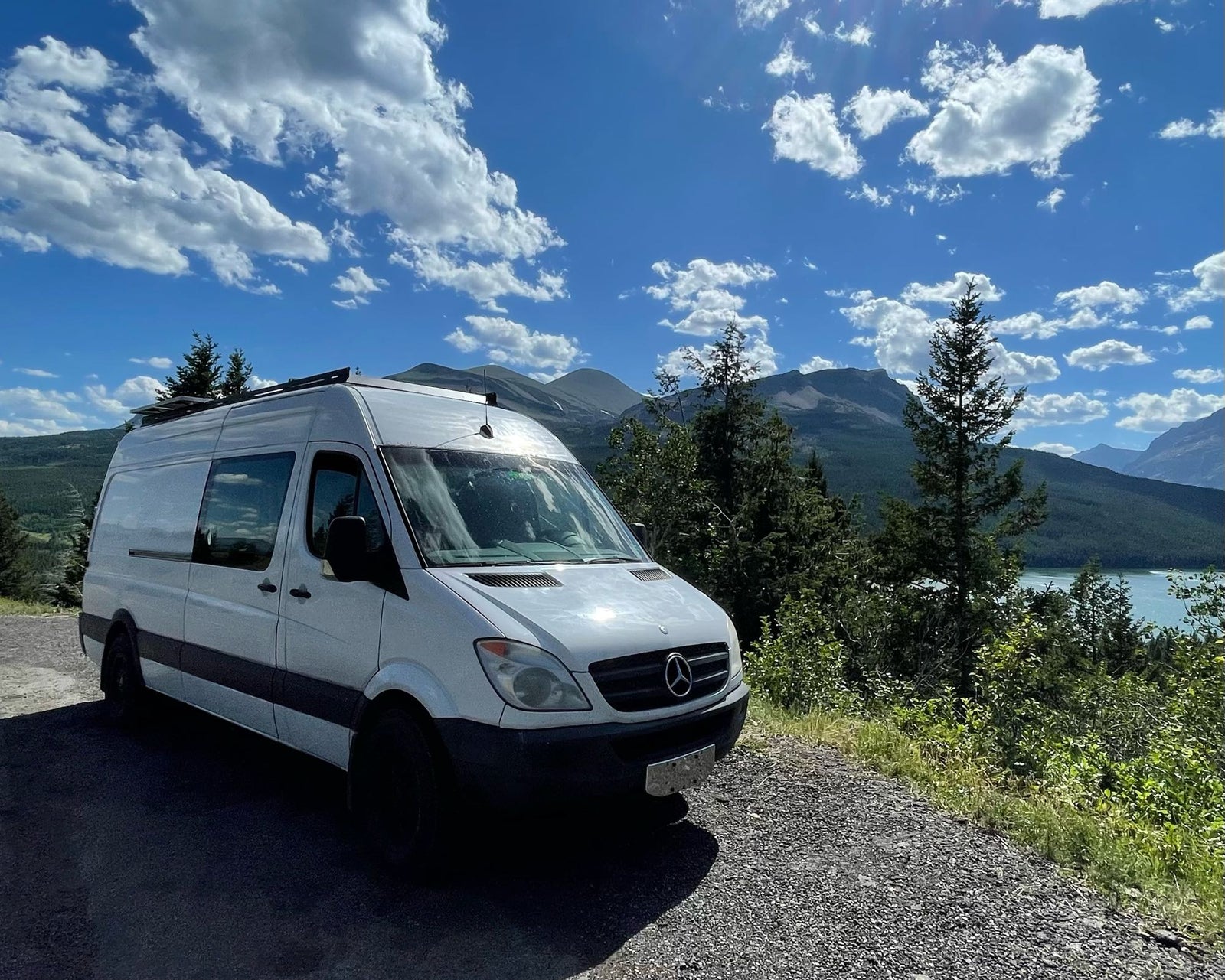 featuring a side ladder & roof setup.|A white rv rental van is parked on a scenic mountain road overlooking a tranquil lake under a blue