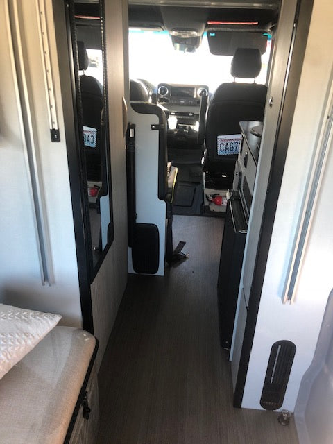 Interior of a sleek rv rental, facing the driver's cabin with a compact kitchen and living area. Ready for road trips!