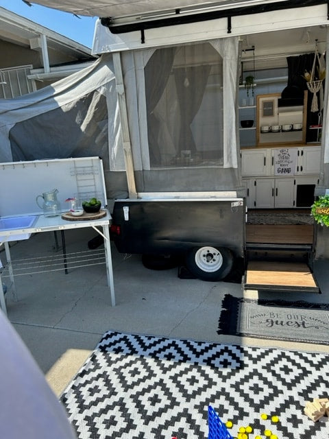 An RV rental, a pop-up camper, fully set up with an outdoor kitchen, patio rug, and interior cabinets visible. — photo 10