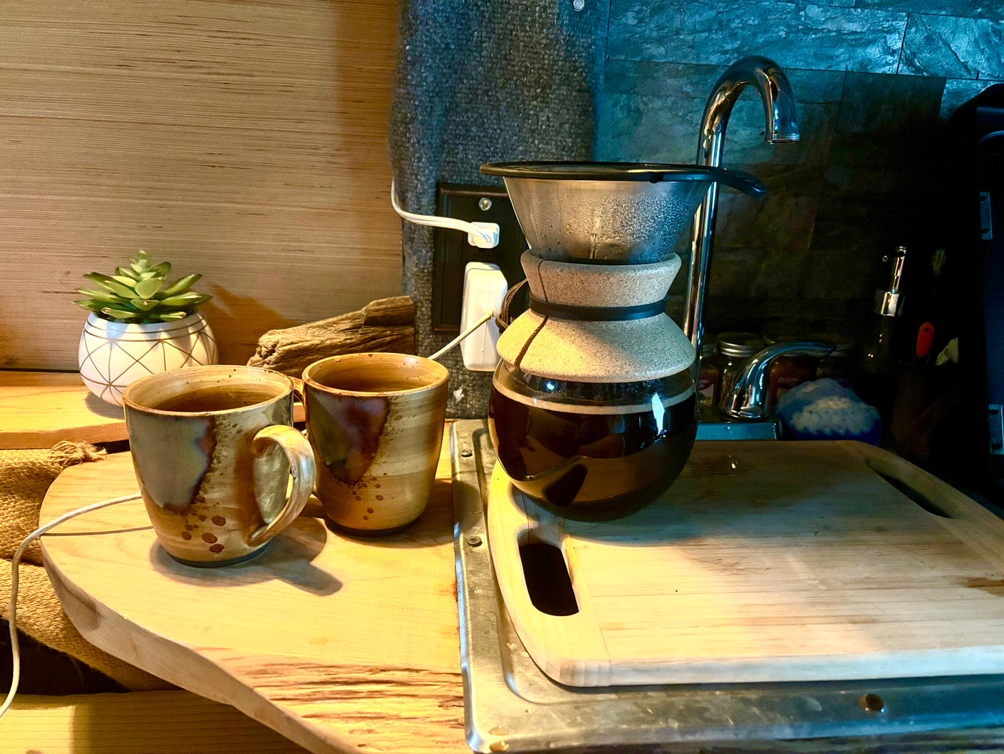 Cozy coffee setup in a compact RV rental kitchen, featuring pour-over coffee, two artisan mugs, and a small plant.