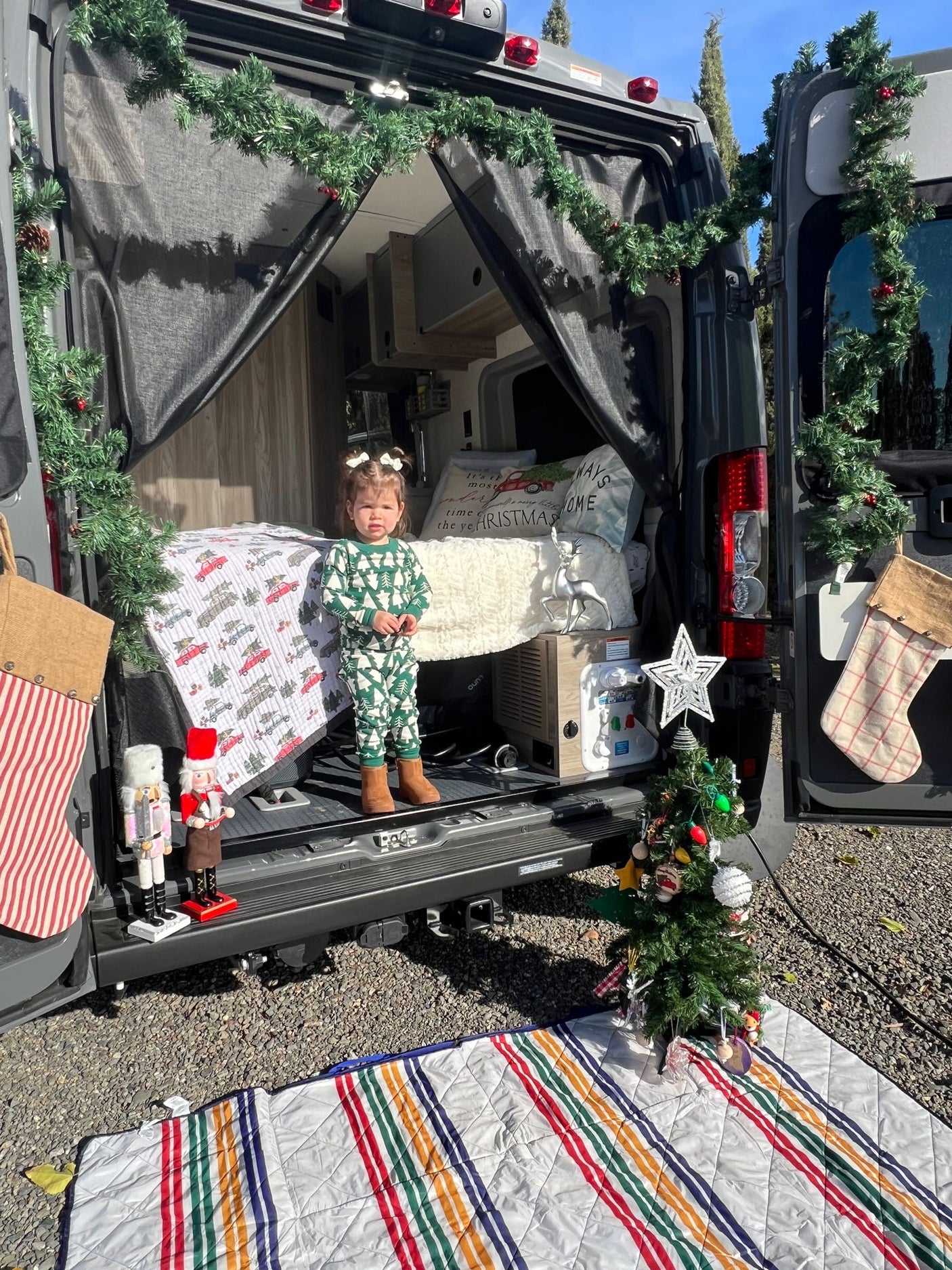 Holiday-ready RV rental: a toddler in Christmas pajamas enjoys the decorated campervan. Perfect for festive family travel!