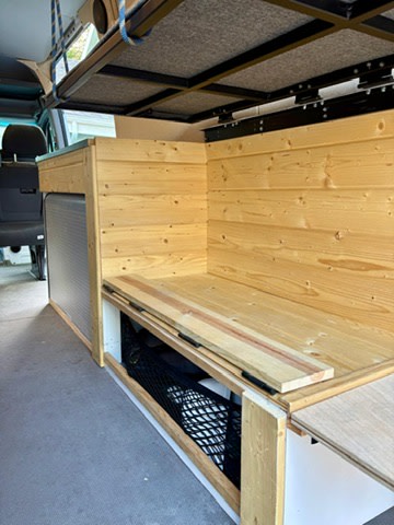 RV rental van conversion: custom wooden bench, backrest, under-seat storage net, and an overhead bed platform.