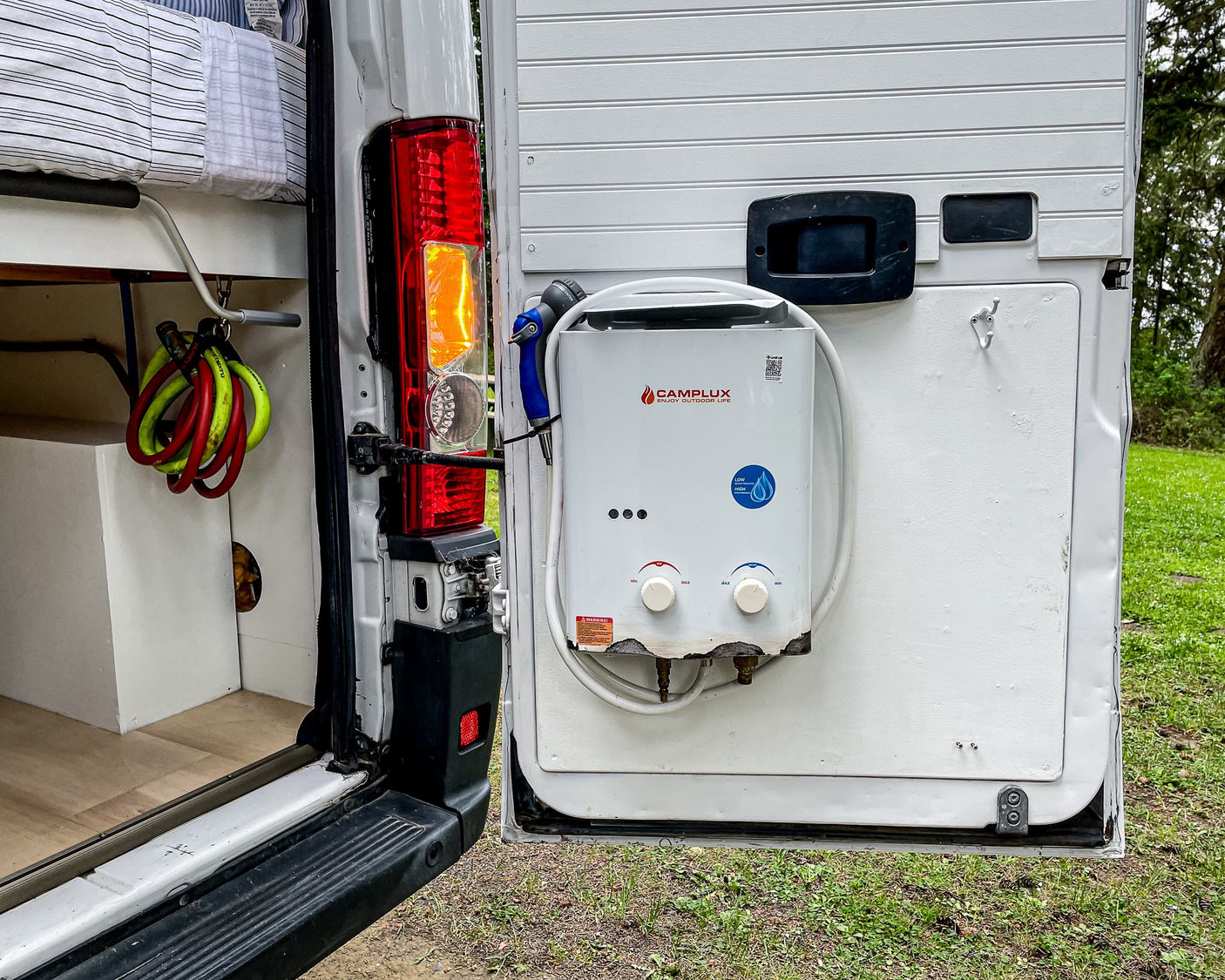 This RV rental's rear door is open, revealing a Camplux portable water heater, shower, and interior storage.