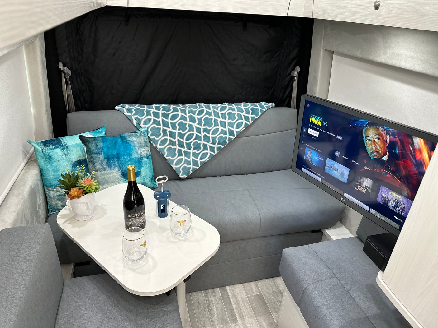 RV rental interior featuring a cozy lounge area with TV, wine, and comfortable seating, ideal for relaxation.