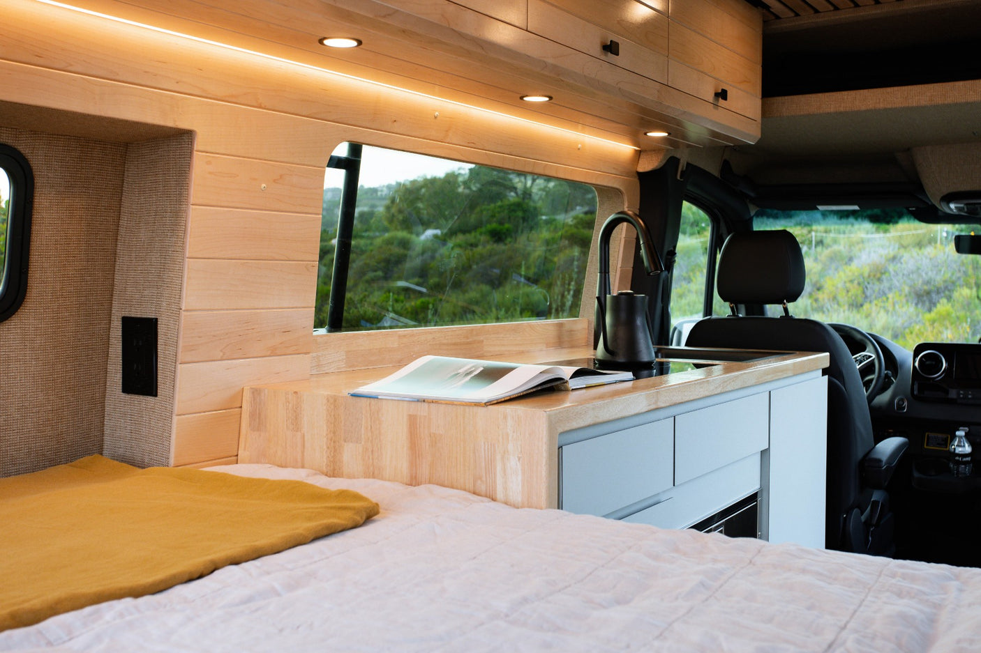 Cozy RV rental interior: compact kitchen, comfortable bed, and scenic window for travel.