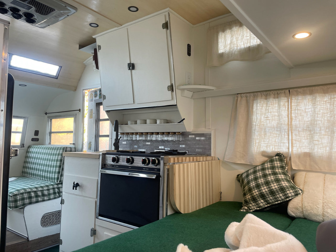 Explore this cozy RV rental's interior: a compact kitchen, green plaid seating, and comfy bed, all ready for your next adventure.