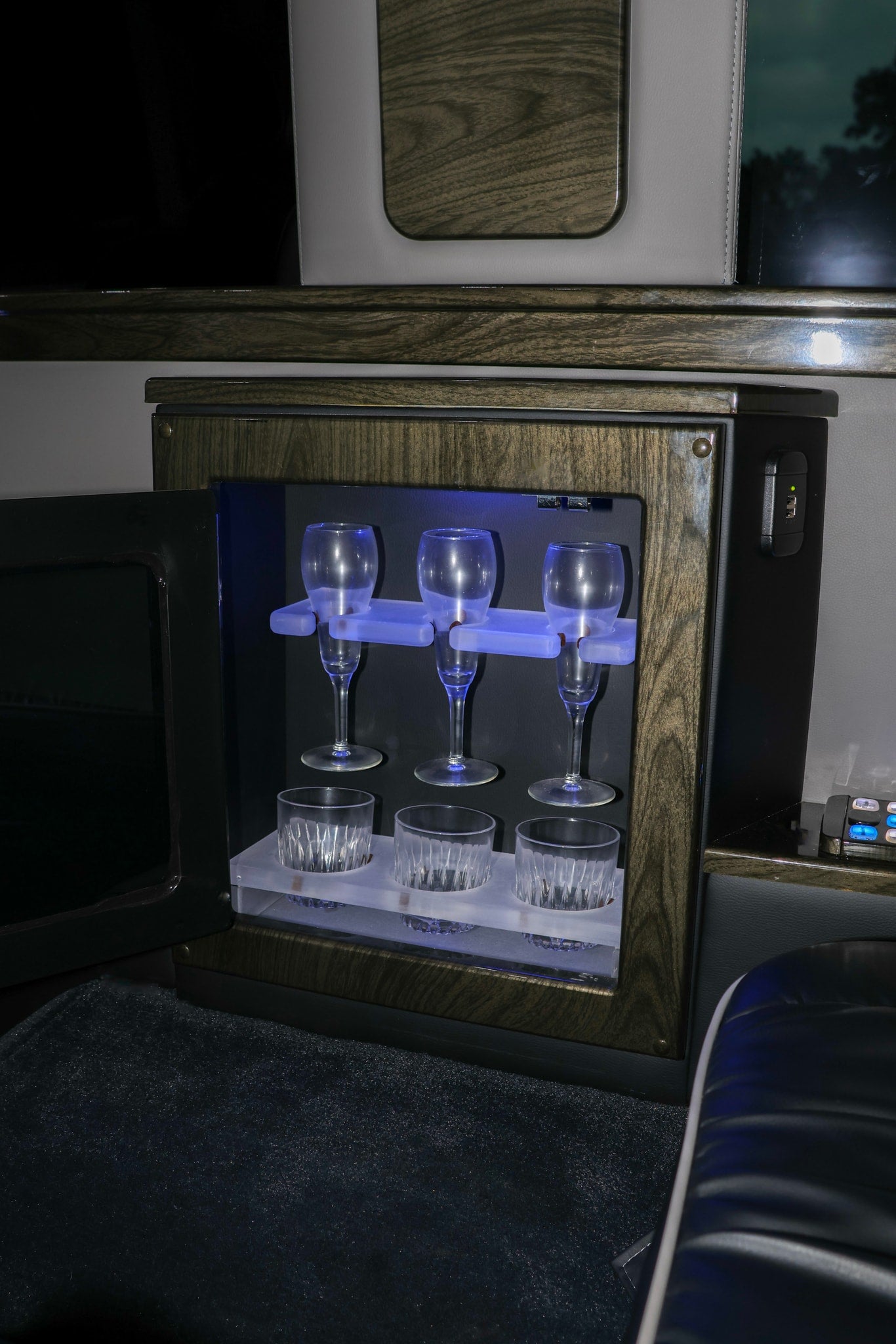 Luxury rv rental interior: an illuminated mini-bar with champagne flutes, whiskey tumblers, and a USB charger.