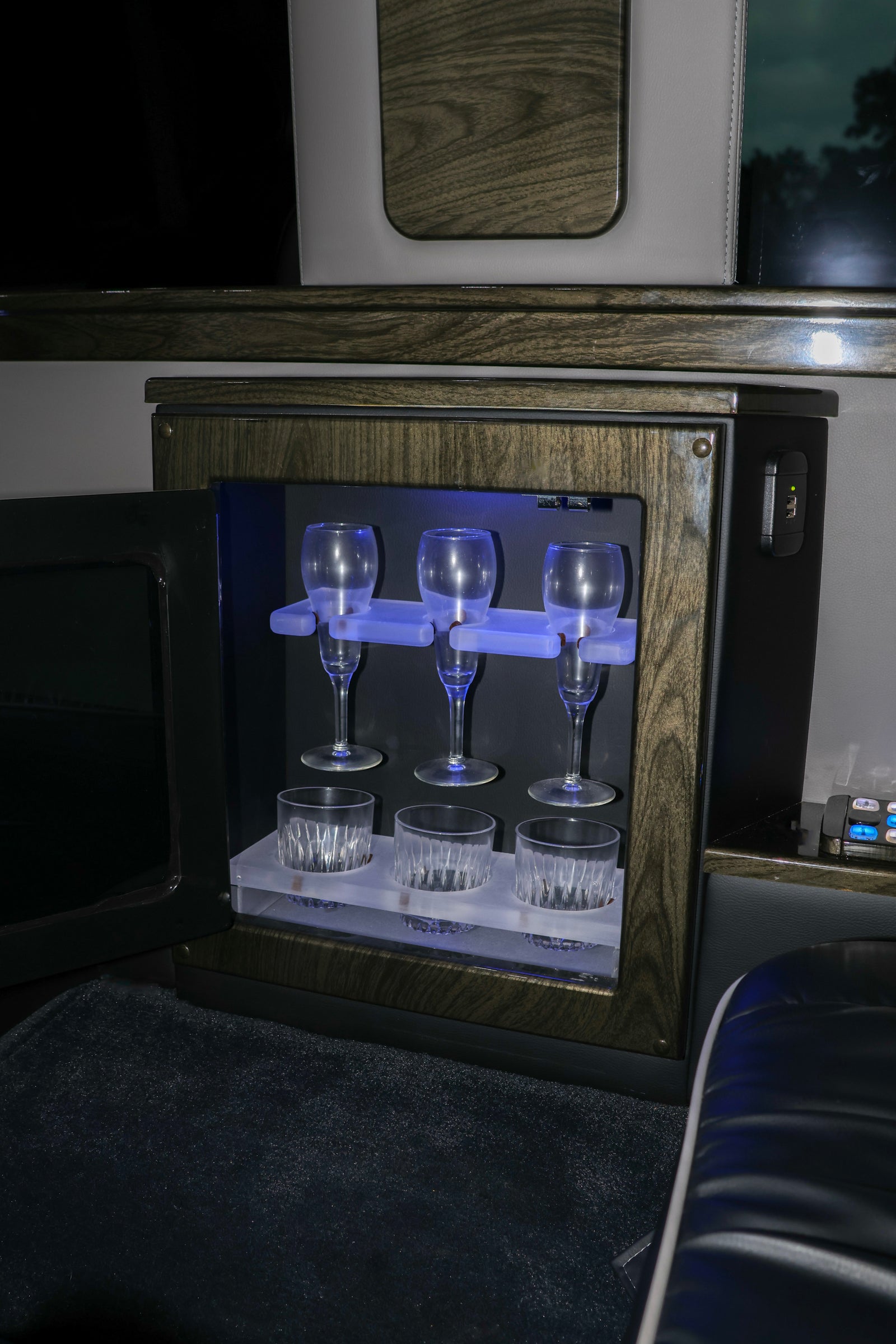Luxury rv rental interior: an illuminated mini-bar with champagne flutes, whiskey tumblers, and a USB charger.