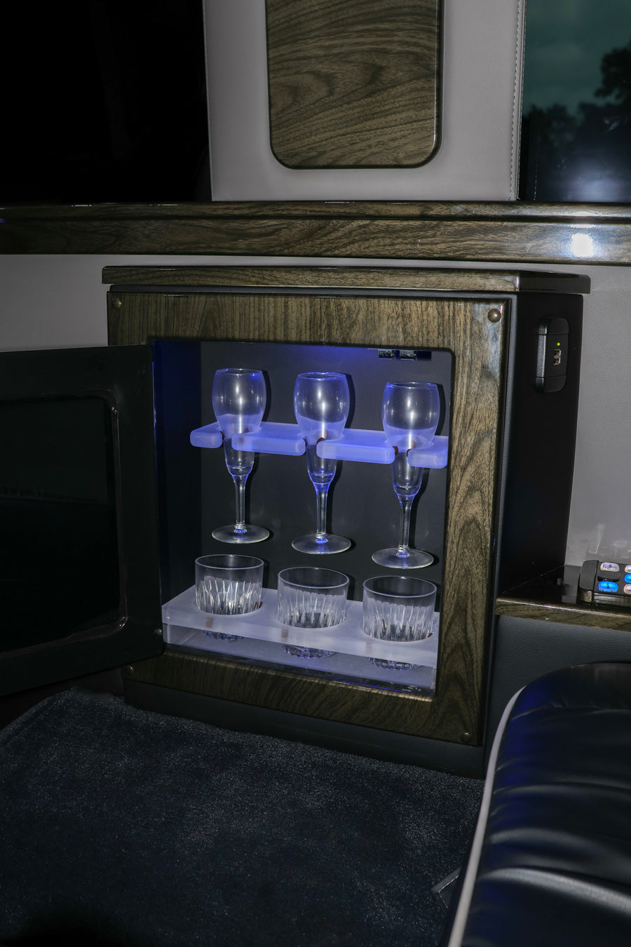 Luxury rv rental interior: an illuminated mini-bar with champagne flutes, whiskey tumblers, and a USB charger.