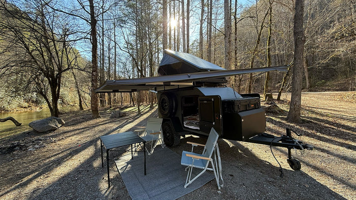 and a scenic view of a river/lake and trees outside the open door.|Riverside rv rental campsite with an off-road camper trailer