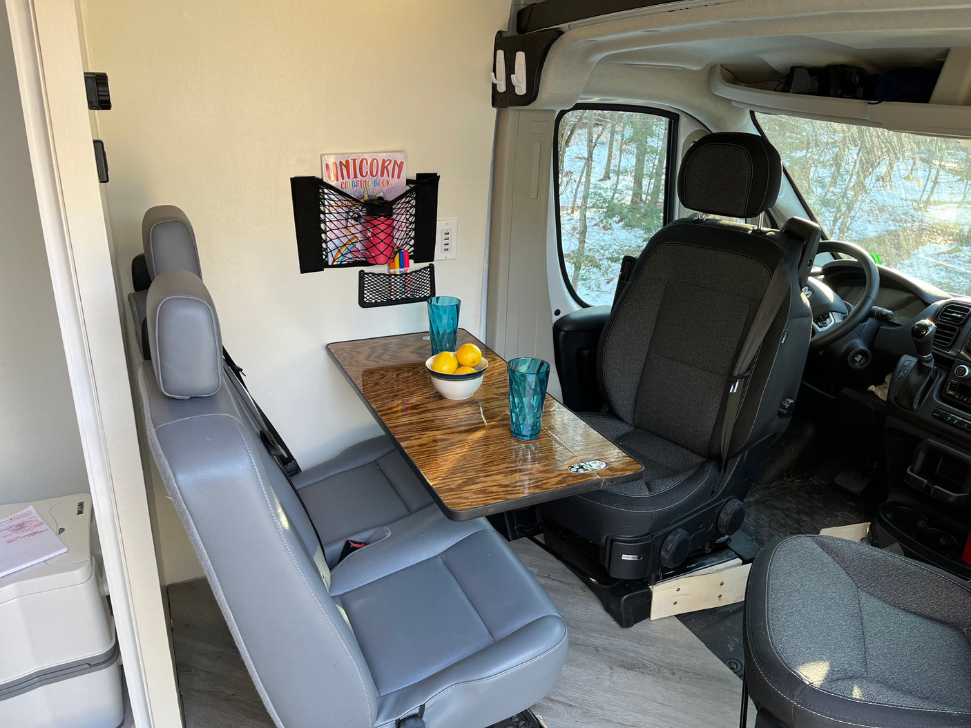 Experience an RV rental! This cozy van interior features a dining area, passenger seating, and a convenient portable toilet.