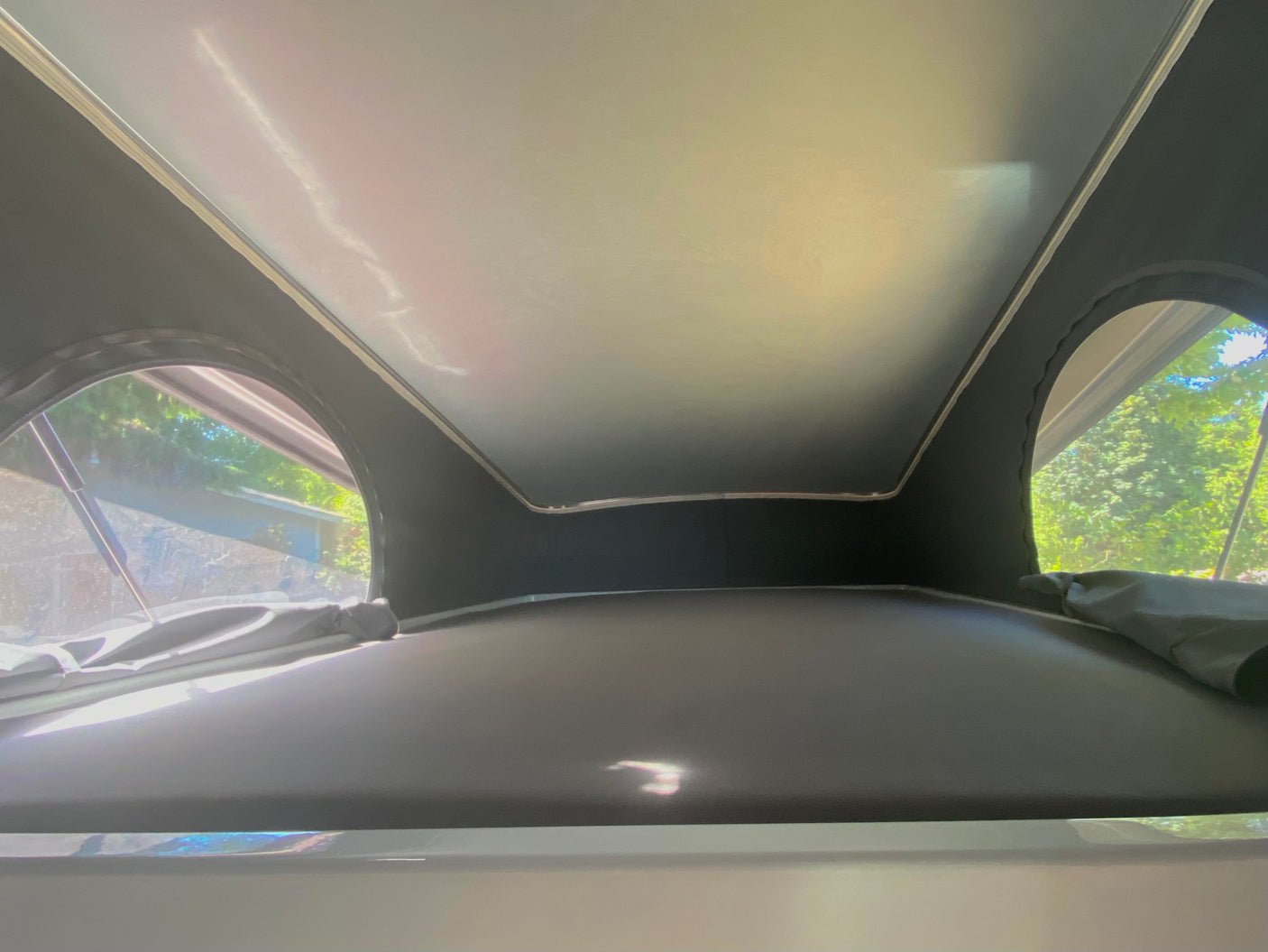 Inside an RV rental pop-top camper: a cozy sleeping platform and arched windows revealing lush trees outside. Bright interior.