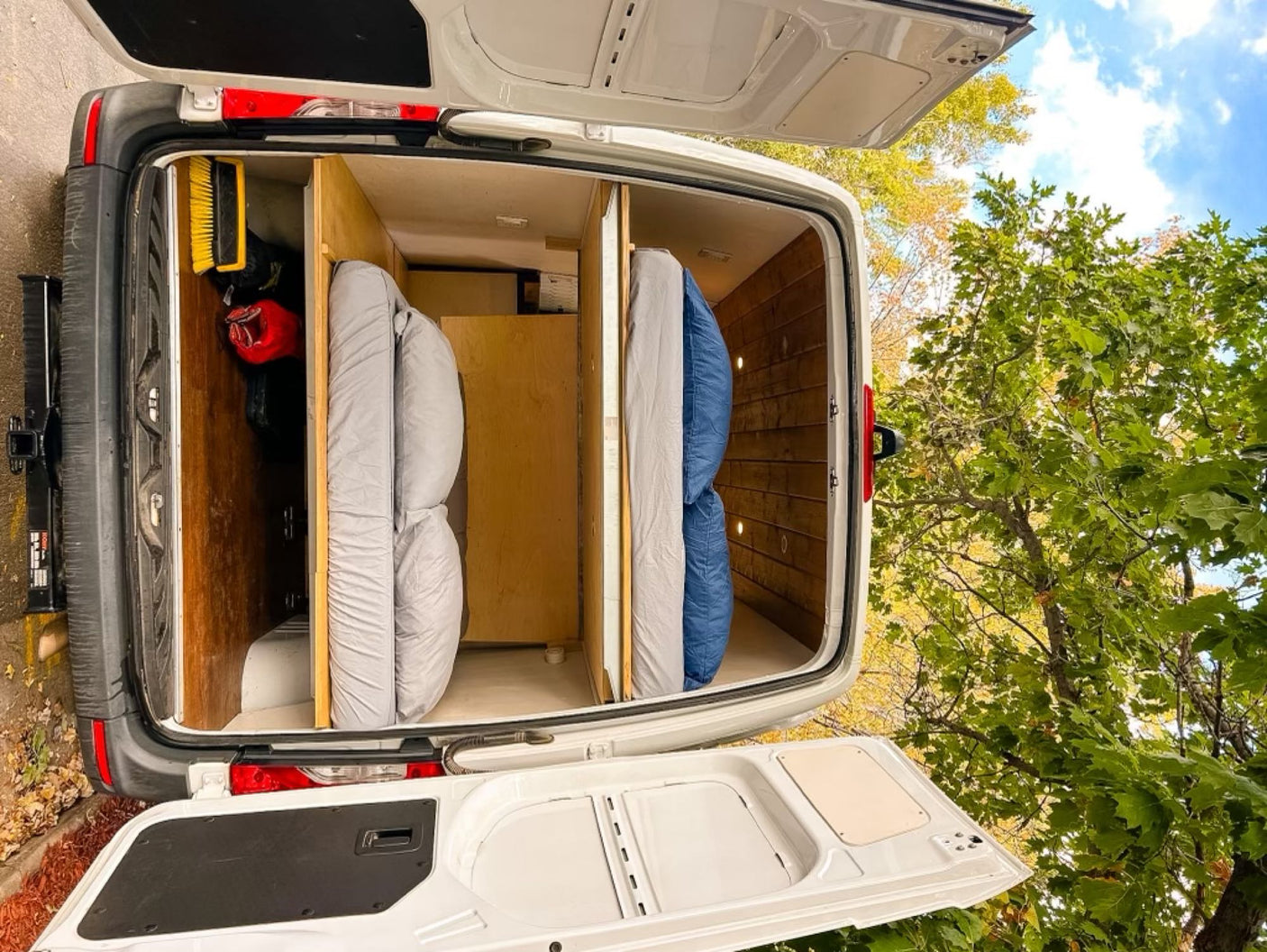 Rear view of an RV rental's camper van interior, featuring two rolled mattresses and wood storage.