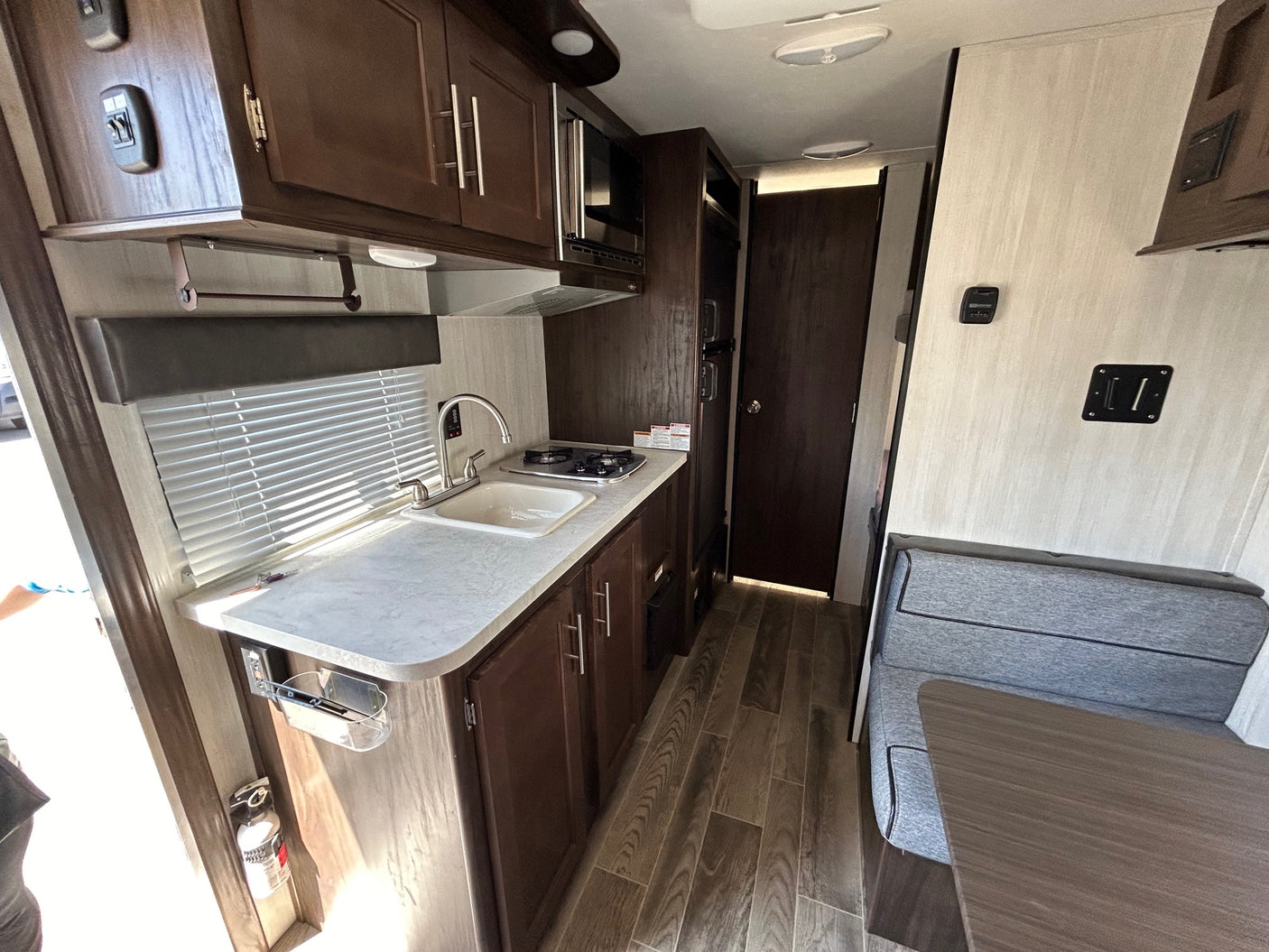 RV rental interior: full kitchen with sink, stovetop, microwave, dark wood cabinets, and dinette seating.
