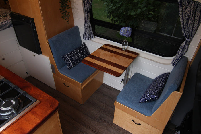 Cozy RV rental interior showcasing a compact dining area with blue benches, a wooden table, and an integrated kitchen.