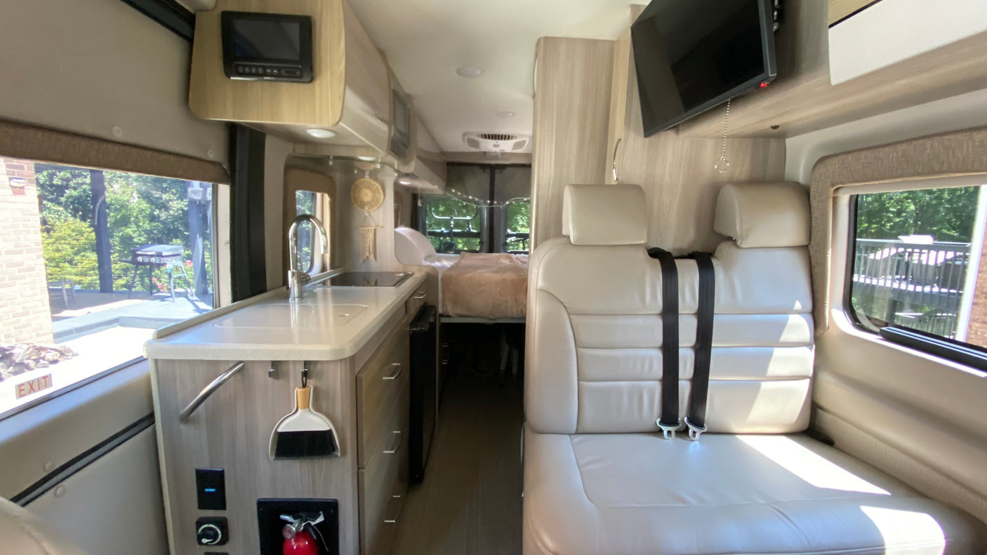 Inside this RV rental: a modern kitchen, comfortable seating with seatbelts, and a cozy rear bed. Ready for your adventure!
