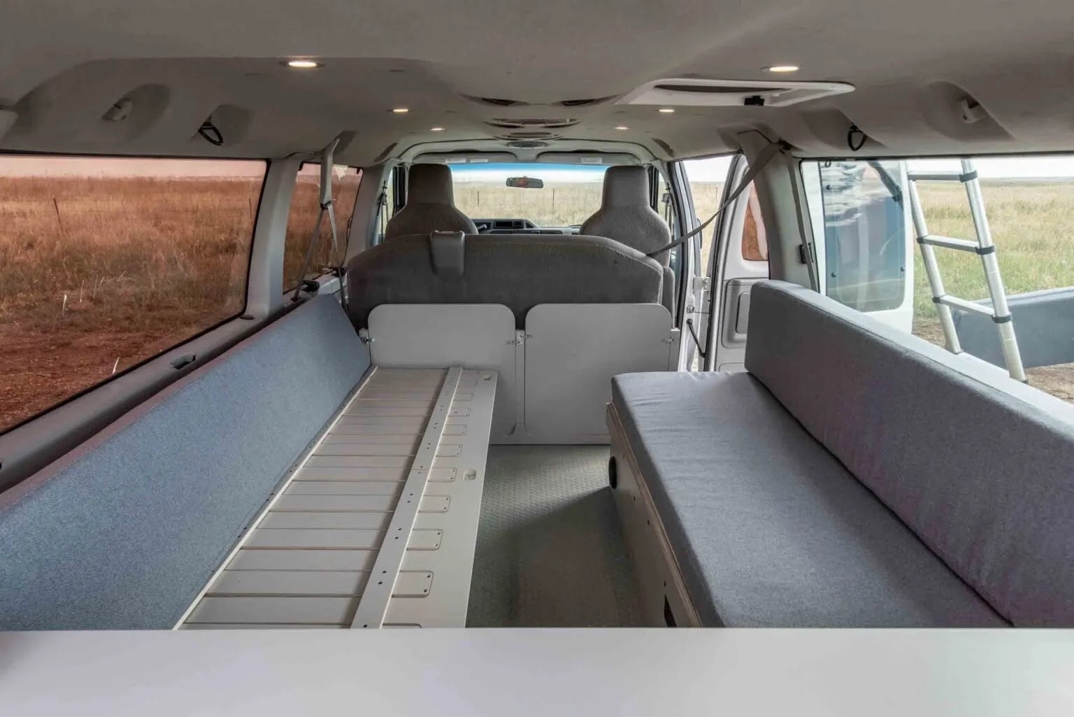 Explore this RV rental's spacious interior: grey cushioned beds/seating, a central platform, and scenic views from the open back door.