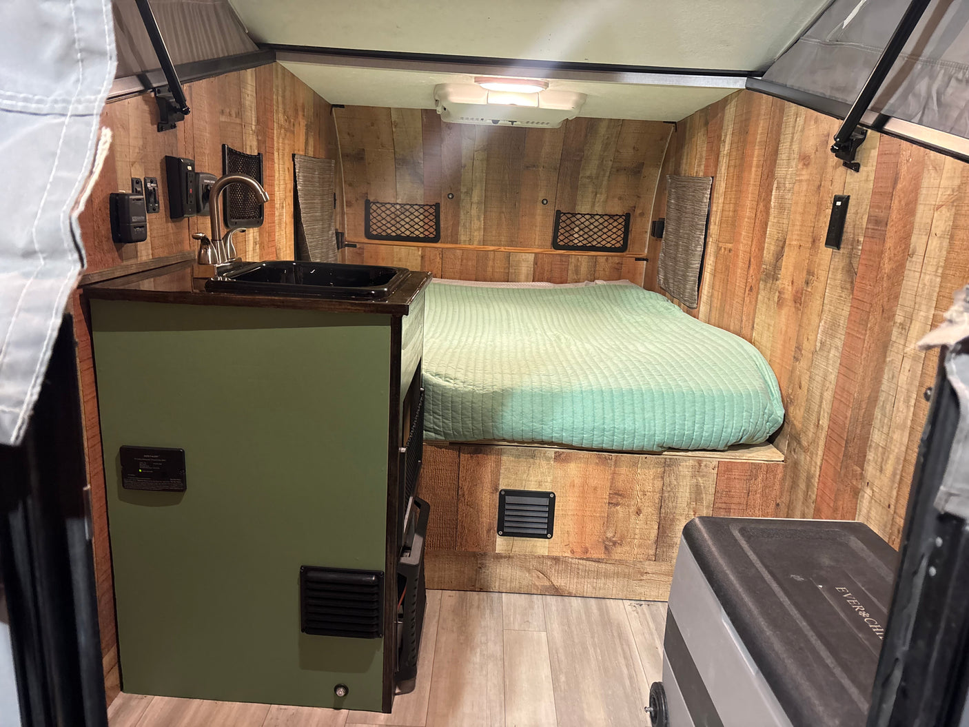 Cozy rv rental interior: green bed, small kitchen sink, wood walls, and control panel, ideal for compact travel.