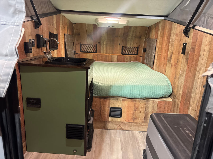 Cozy rv rental interior: green bed, small kitchen sink, wood walls, and control panel, ideal for compact travel.