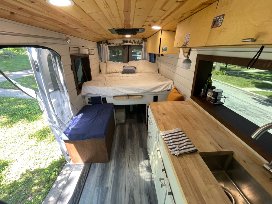 Cozy RV rental interior, showcasing a comfortable bed, compact kitchen, and warm wood accents. Perfect for a road trip.