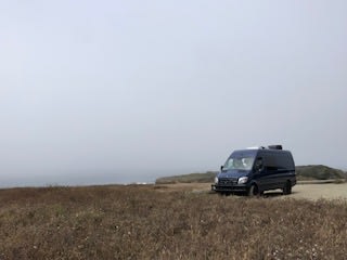 A dark rv rental camper van sits on a brown field under a foggy sky, ready for a road trip or serene van life. — photo 20