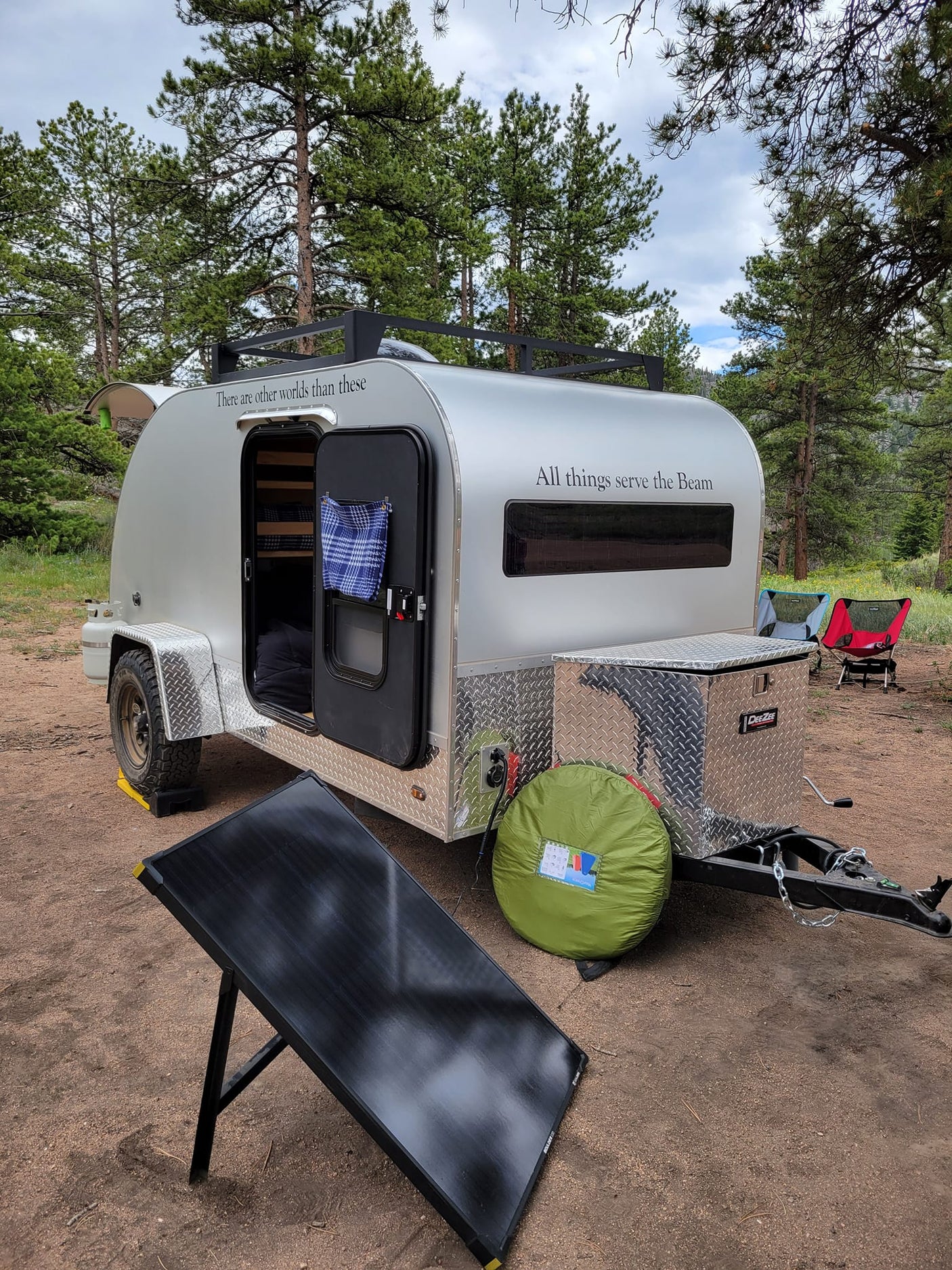 Cozy teardrop rv rental parked at a serene campsite, powered by a large solar panel, ideal for nature escapes.