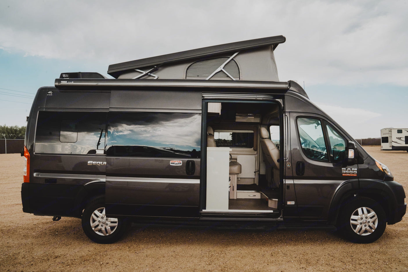 Grey camper van with an extended pop-top and open side door revealing the interior. Great for an rv rental.