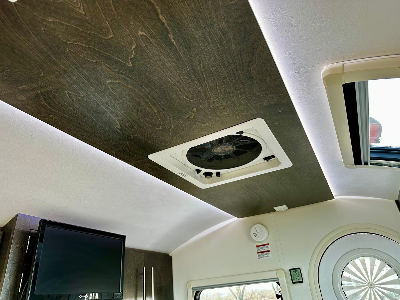 Modern RV rental interior: dark wood ceiling with vent, ambient lighting, TV, and climate display for comfortable travel.