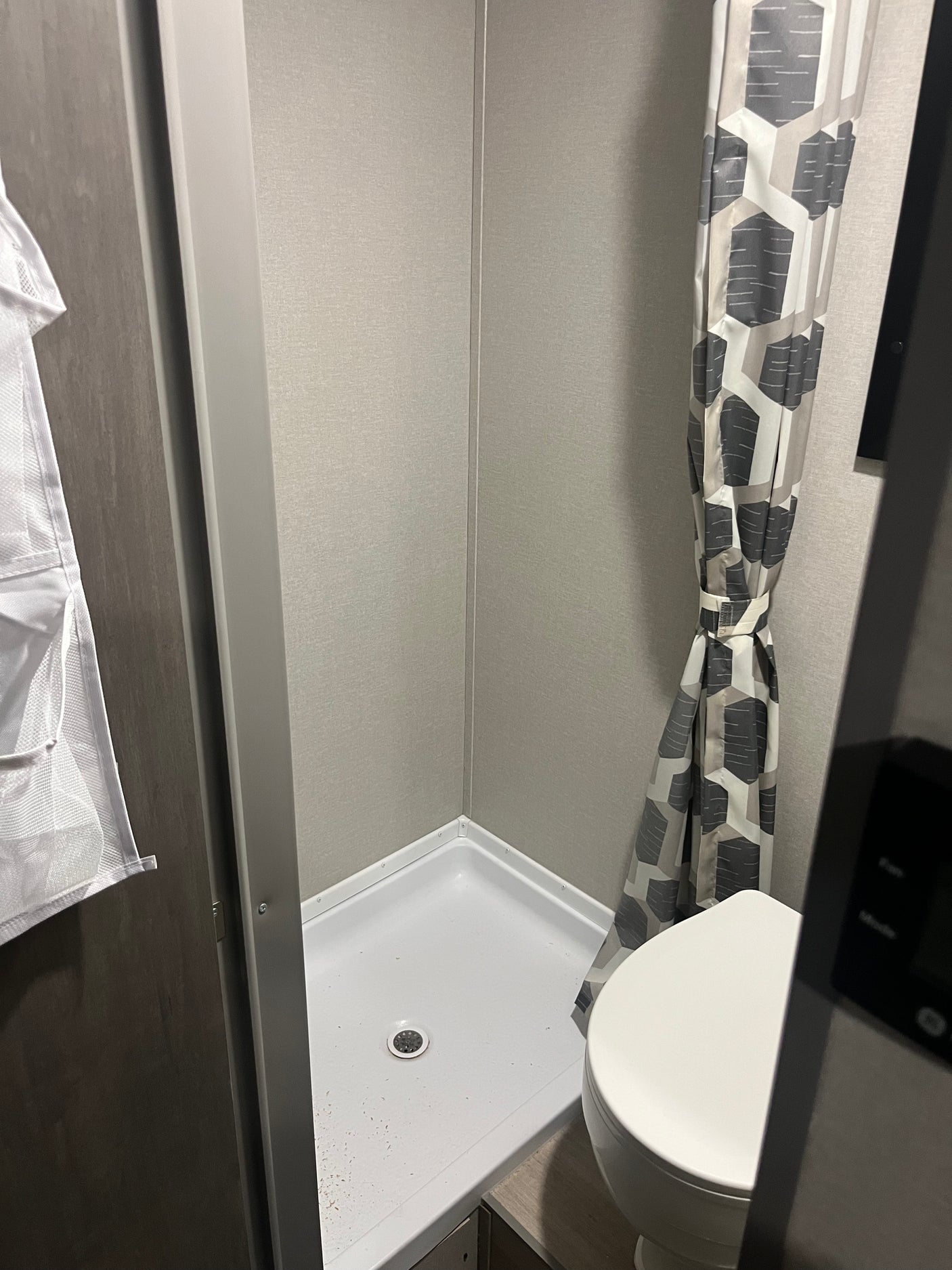 Inside a compact RV rental bathroom: shower stall with white pan, drain, and gray walls, plus a toilet and patterned shower curtain.