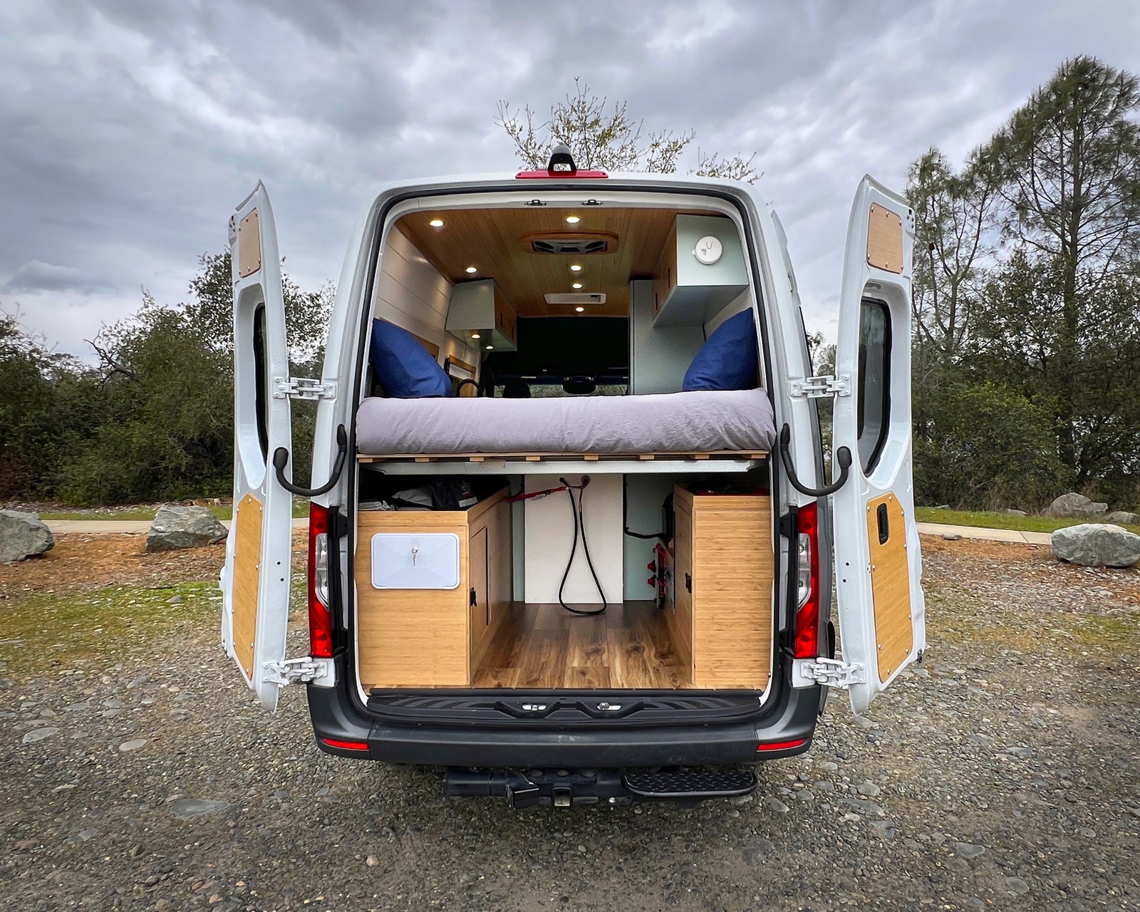 Explore in comfort! This RV rental offers a well-appointed camper van interior, featuring a bed & storage, seen with open doors.