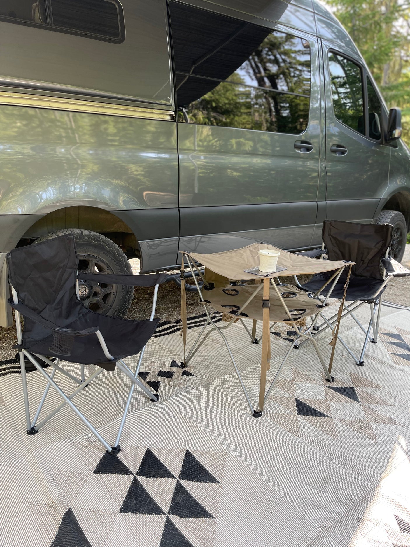 Relaxing at camp with our RV rental! Features a gray camper van, outdoor rug, comfy chairs, and folding table.