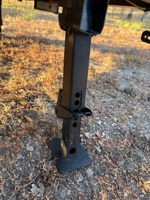 RV rental jack securely deployed on dry ground. The black metal stabilizer leg features adjustment holes for precise leveling.