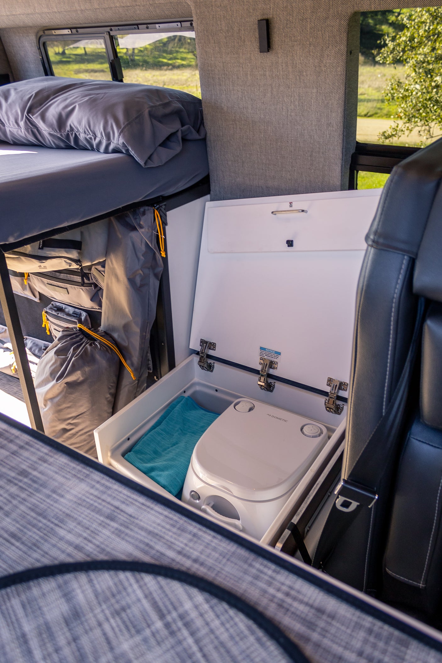 Compact RV rental interior: bed, organized storage, and a discreet Dometic portable toilet. Adventure ready.