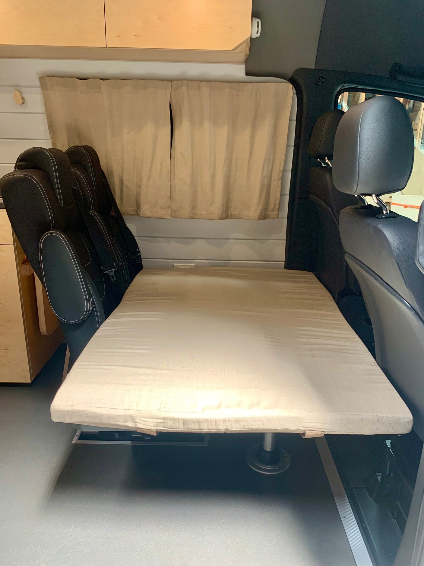 RV rental features: A versatile van interior showing a flat bed or seating area, with black passenger seats & light wood cabinets.