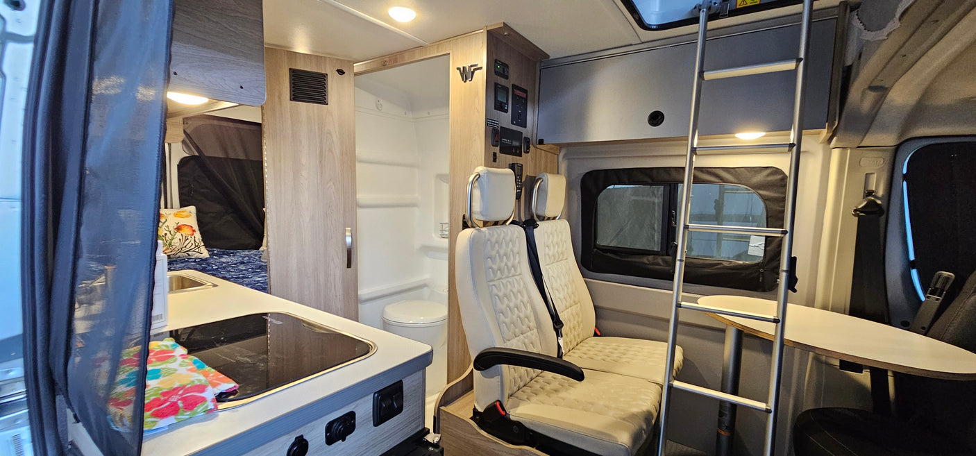 This RV rental interior offers a kitchen area, compact bathroom, bed, and flexible seating with an upper bunk ladder.