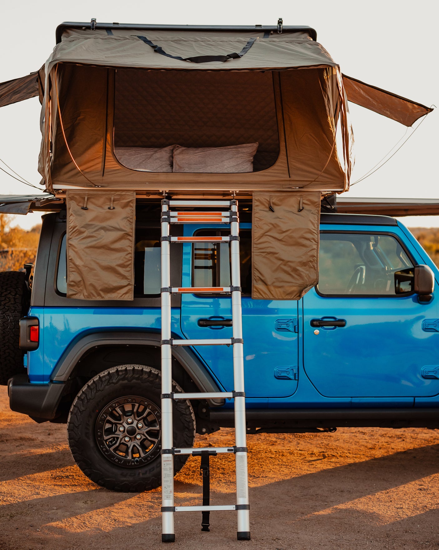 This blue Jeep, equipped with a rooftop tent and ladder, is set up for an outdoor adventure. Explore similar RV rental camping experiences!