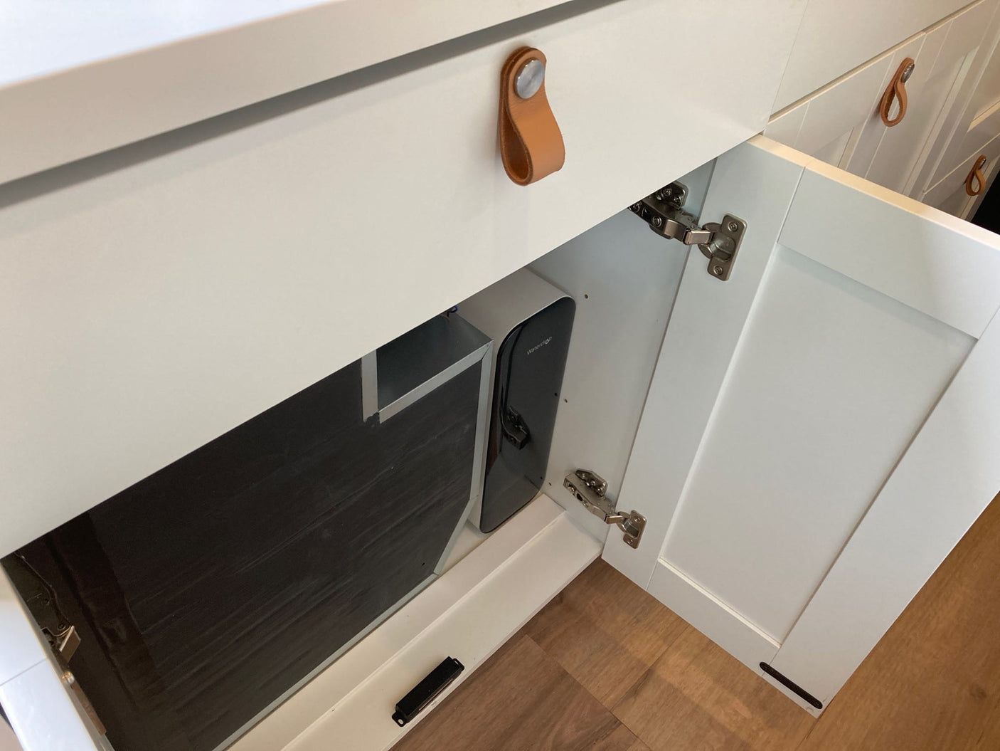 RV rental kitchen: open white cabinet reveals a compact Waterdrop water filter and dark pull-out storage.